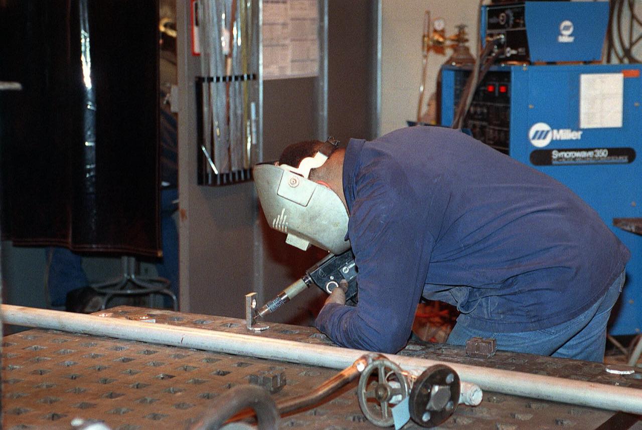 A worker welding a steel brace in a machine shop